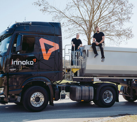 Zwei LKW-Fahrer von Innoko sitzen auf Ladefläche eines Innoko LKW und lächeln in die Kamera
