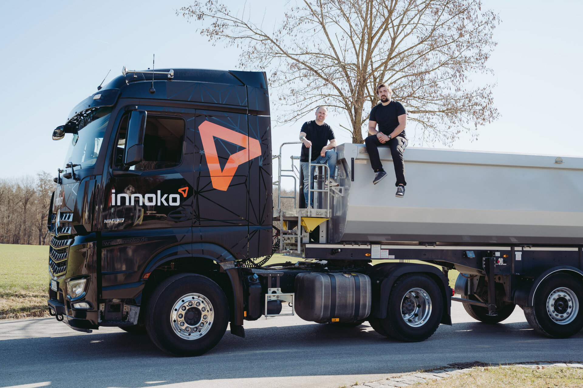 Zwei LKW-Fahrer von Innoko sitzen auf Ladefläche eines Innoko LKW und lächeln in die Kamera